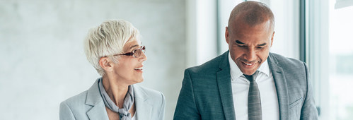 Two smiling business people walking through office hall and talking